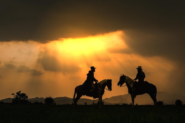 Silhouette von Cowboys, die bei Sonnenuntergang auf einem bewölkten Himmel reiten