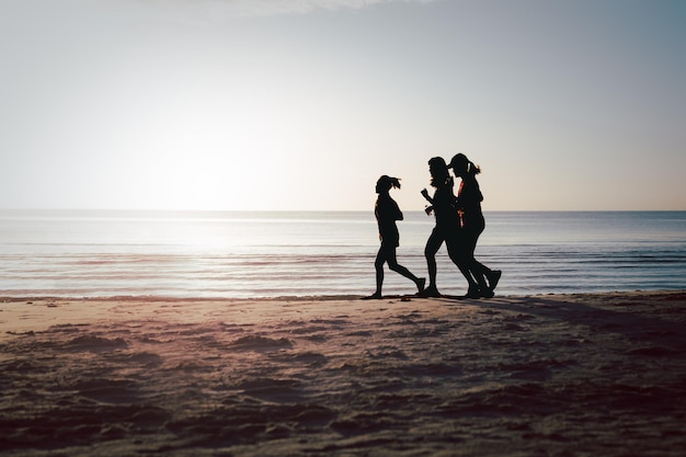 Silhouette von drei Frauen, die bei Sonnenaufgang am Strand joggen