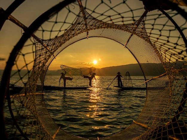 Silhouette von drei traditionellen birmanischen Fischern am Inle-See bei Sonnenuntergang in Myanmar