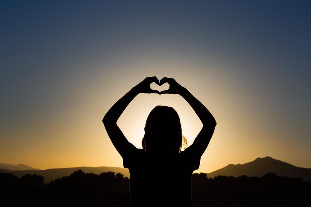 Foto silhouette von einer frau, die bei sonnenuntergang in herzform gegen den himmel steht