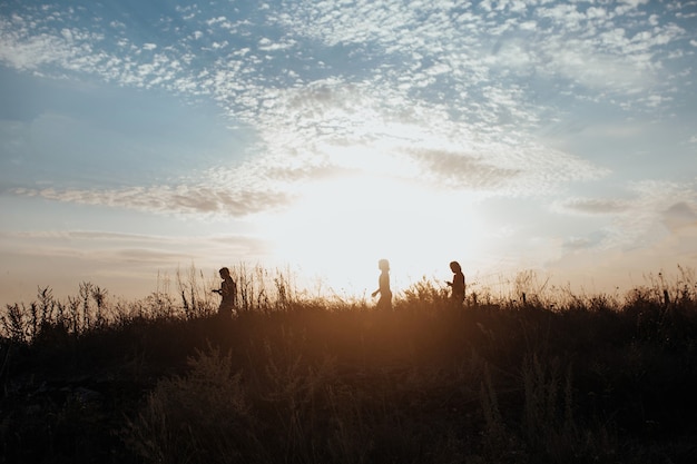 Silhouette von Kindern, die bei Sonnenuntergang über das Feld laufen