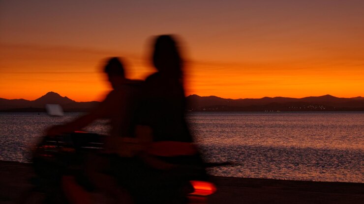 Foto silhouette von menschen, die am meer gegen einen orangefarbenen himmel stehen.