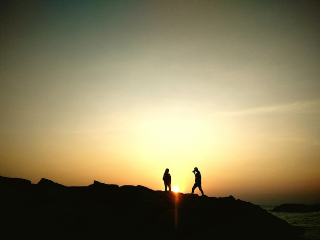 Foto silhouette von menschen, die auf einer klippe am meer gegen einen klaren himmel stehen