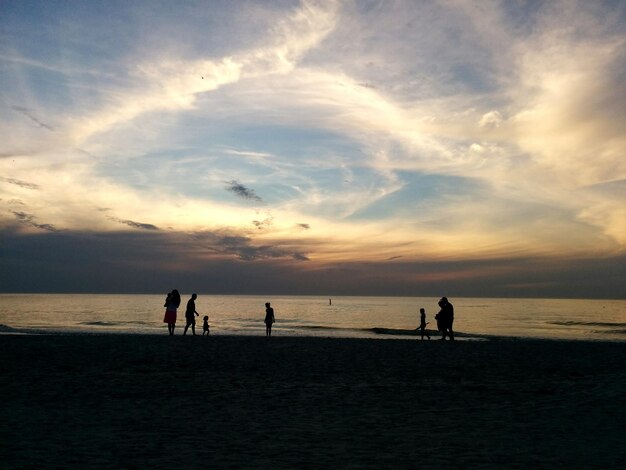 Silhouette von Menschen, die bei Sonnenuntergang am Strand gegen den Himmel laufen