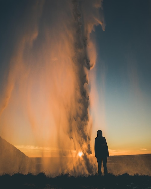 Silhouette von Menschen, die bei Sonnenuntergang neben einem Wasserfall stehen