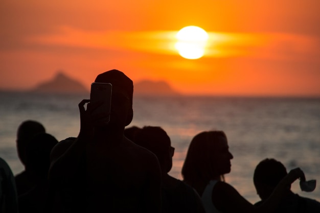 Silhouette von menschen, die den sonnenuntergang am arpoador beach in rio de janeiro, brasilien beobachten.