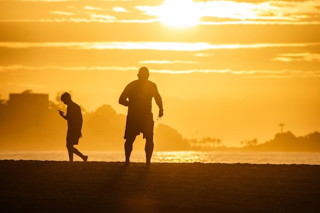 Silhouette von Menschen, die im Morgengrauen am Strand von Leblon in Rio de Janeiro laufen