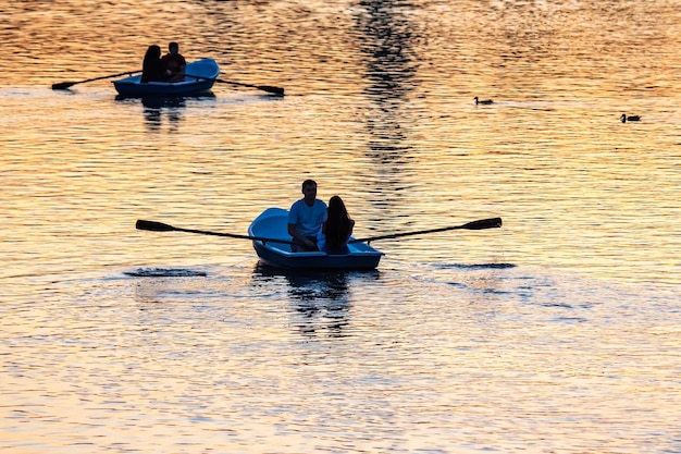 Silhouette von Menschen in Booten mit Rudern am abendlichen Fluss