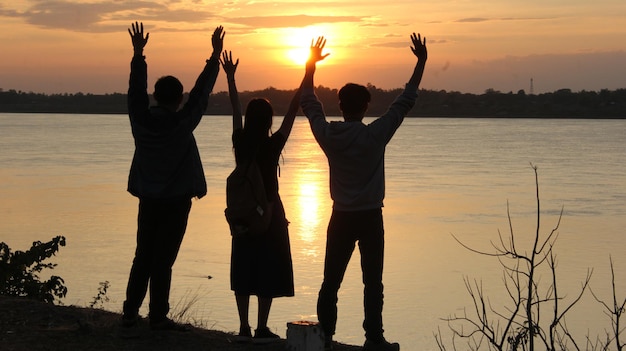 Foto silhouette von menschen mit erhobenen armen, die bei sonnenuntergang am see stehen