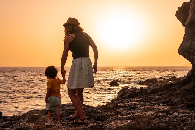 Silhouette von Mutter und Sohn, die in den Sonnenuntergang am Strand von Tacoron auf El Hierro Kanarische Inseln gehen. Urlaubskonzept orangefarbener Sonnenuntergang