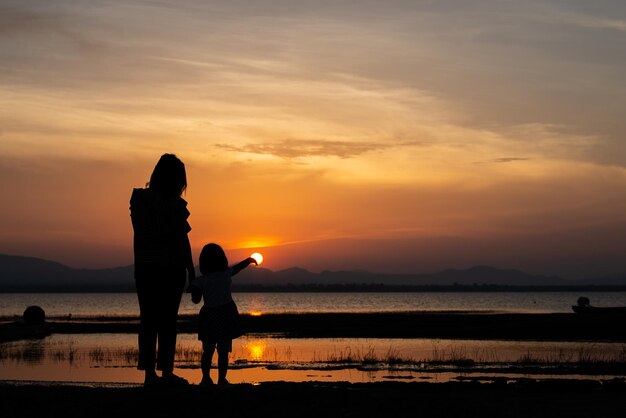 Silhouette von Mutter und Tochter am Meer bei Sonnenuntergang