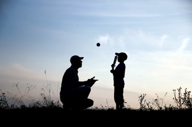 Silhouette von Vater und Sohn, die Baseball auf dem Naturfamiliensportkonzept spielen