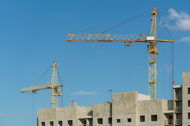 Silhouetten arbeitender Baukranen vor dem Hintergrund eines unvollendeten Wohngebäudes, eines mehrstöckigen Luxuswohnungsgebäudes auf einer Baustelle