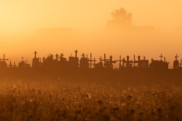 Silhouetten der Kreuze des katholischen Friedhofs im Nebel am frühen Morgen in der Morgendämmerung Platz für Ihren Text