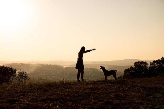 Silhouetten einer entzückenden Frau, die während des Sonnenuntergangs mit ihrem süßen Hund läuft