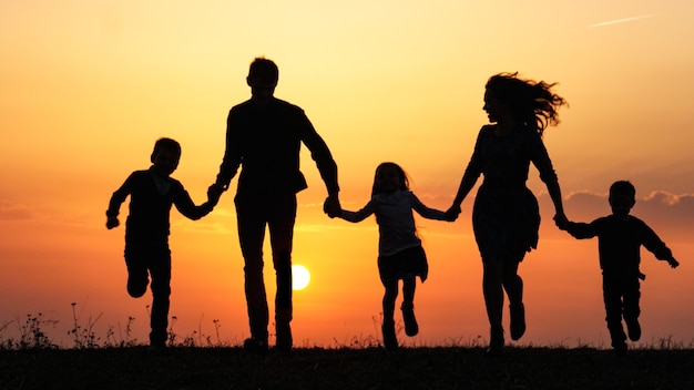 Foto silhouetten einer glücklichen familie, die bei sonnenuntergang die hände auf der wiese hält
