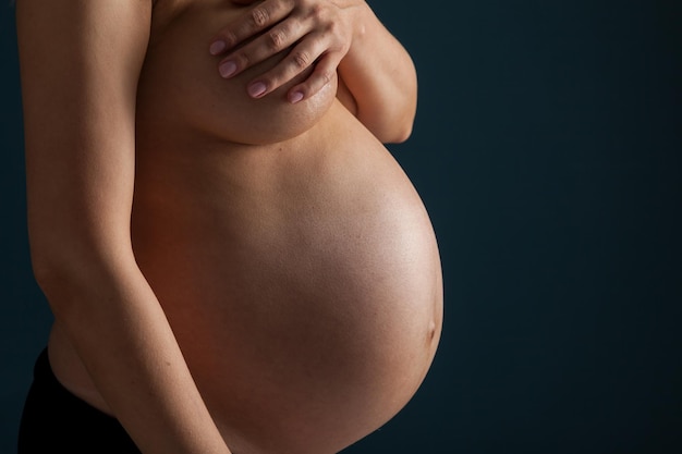 Silhouetten einer schwangeren schönen Frau, die nackt oben ohne ist und ihre Brust mit einem dicken Bauch bedeckt, in Erwartung der Geburt eines Kindes