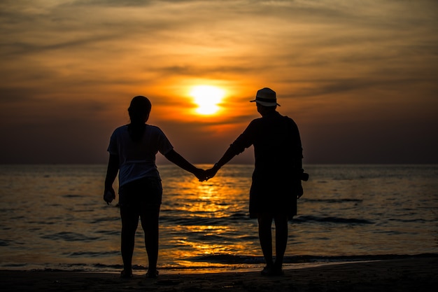 Silhouetten stehen am Meer und orange Himmel.