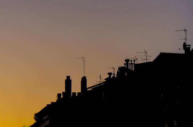 Silhouetten von Antennen, Schornsteinen und Dächern unter einem Sonnenunterganghimmel