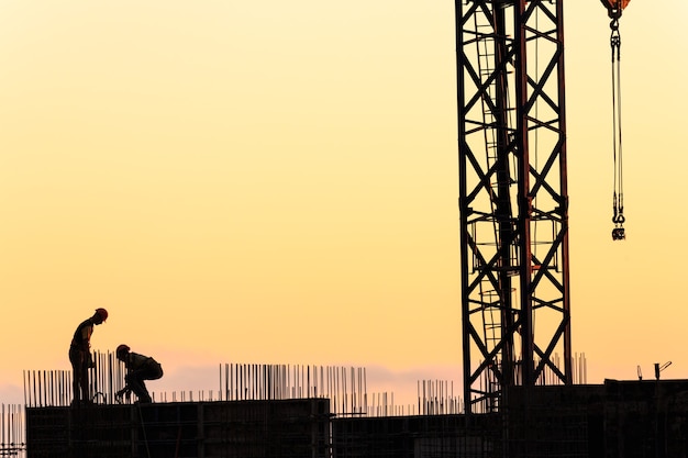 Silhouetten von Arbeitern beim Bau eines Wolkenkratzers vor dem Hintergrund des Sonnenuntergangshimmels
