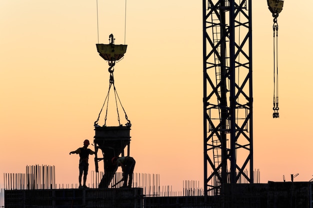 Silhouetten von Arbeitern beim Bau eines Wolkenkratzers vor dem Hintergrund des Sonnenuntergangshimmels