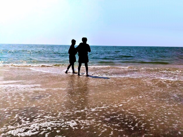 Foto silhouetten von männern, die an einem sonnigen tag am strand gegen einen klaren himmel stehen