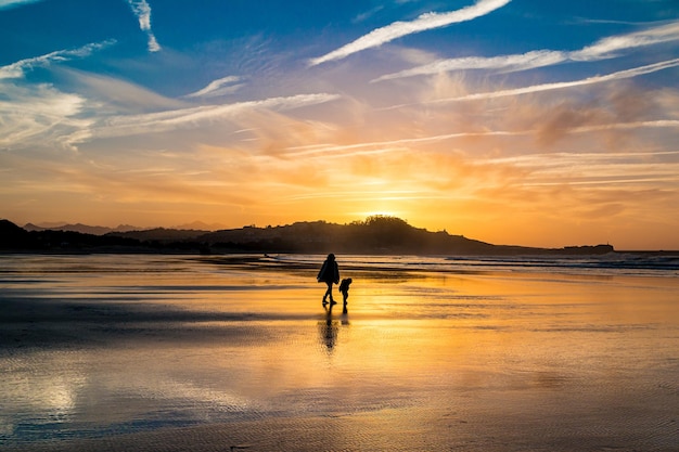 Silhouetten von mutter und kind, die während des atemberaubenden sonnenuntergangs an einem wintertag an einem strand spazieren