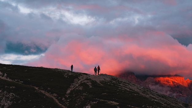 Silhouetten von Wanderern auf einem Hügel unter einem bewölkten Himmel bei einem wunderschönen Sonnenuntergang am Abend