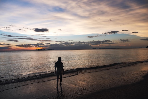 Silhouettenbild einer Frau, die vor Sonnenuntergang im Meer spazieren geht