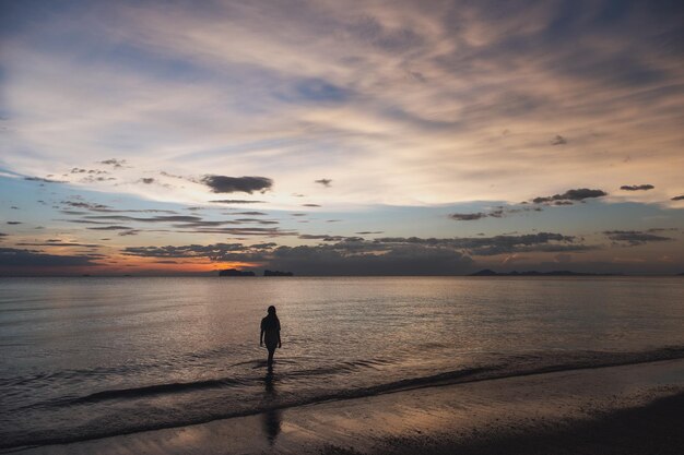 Silhouettenbild einer Frau, die vor Sonnenuntergang im Meer spazieren geht