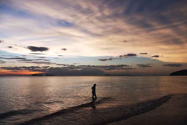 Silhouettenbild einer Frau, die vor Sonnenuntergang im Meer spazieren geht