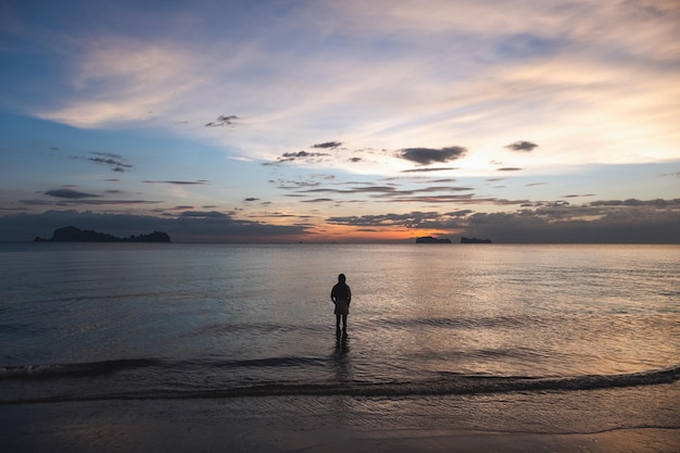 Silhouettenbild einer Frau, die vor Sonnenuntergang im Meer spazieren geht