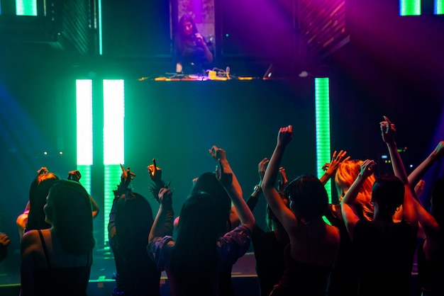 Silhouettenbild von Menschen, die im Disco-Nachtclub zu Musik von DJ auf der Bühne tanzen