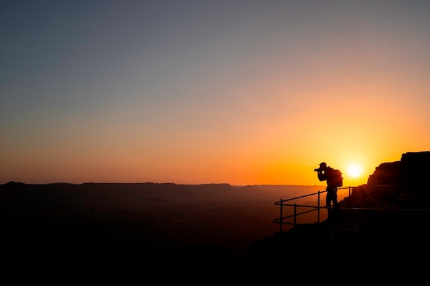 Silhouettenfotograf, der einen Sonnenuntergang in den Bergen schießt. Fotografenkonzept