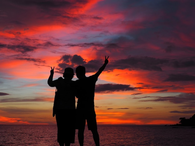 Silhouettenpaar steht am Strand gegen den orangefarbenen Himmel