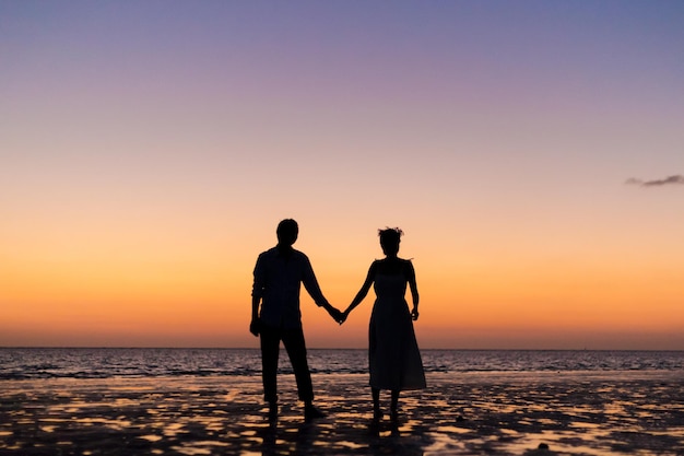 Silhouettenpaar steht bei Sonnenuntergang am Strand vor dem Himmel