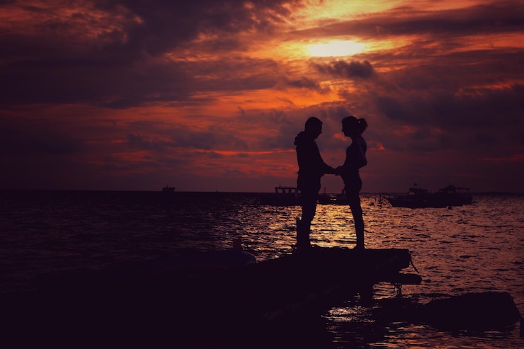 Foto silhouettenpaar steht bei sonnenuntergang am strand vor einem bewölkten himmel