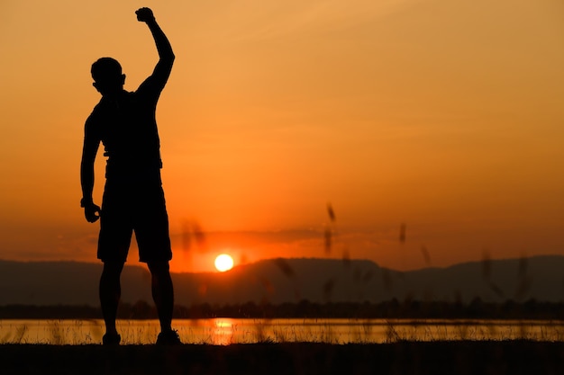 Silhouettensonnenuntergang eines glücklichen, fröhlichen Mannes, der springt und Spaß hat, das Konzept des Kampfes um den Geschäftserfolg des Sieges Freiheit