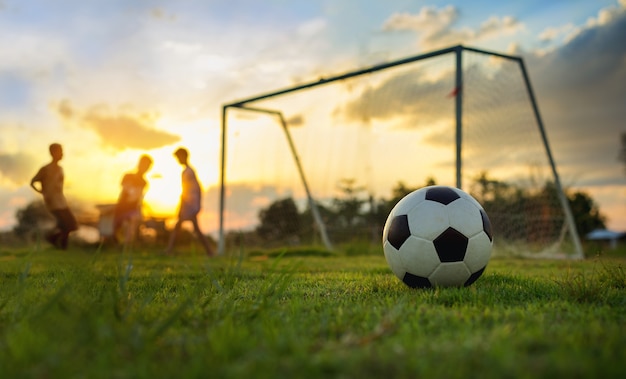 Silhouettieren Sie Aktionsbild einer Gruppe Kinder, die Fußballfußball für Übung spielen.