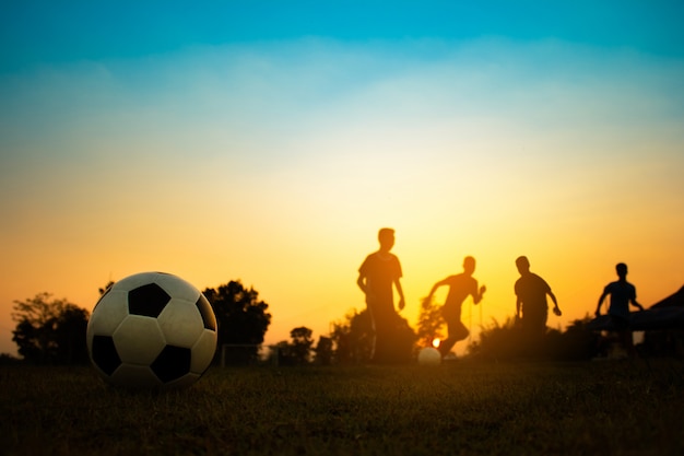 Silhouettieren Sie Aktionssport draußen einer Gruppe Kinder, die den Spaß haben, Fußballfußball zu spielen