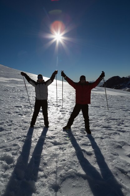 Silhouettieren Sie die Paare, die Hände mit Skipfosten auf Schnee anheben