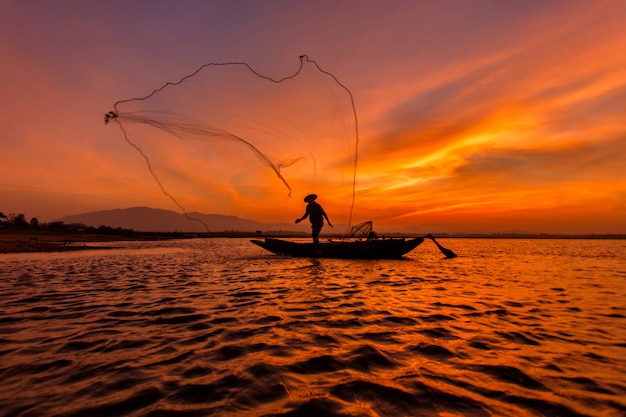 Silhouettieren Sie Fischer mit Netz am See in Thailand