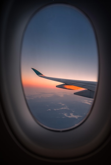 Silhouettieren Sie Flügel eines Flugzeuges an der Sonnenaufgangansicht durch das Fenster.