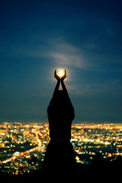 Silhouettieren sie frauenporträt mit vollmond im stadtnachtlicht bokeh hintergrund