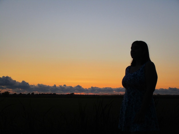 Foto silhueta de una adolescente de pie en el campo contra el cielo durante la puesta de sol
