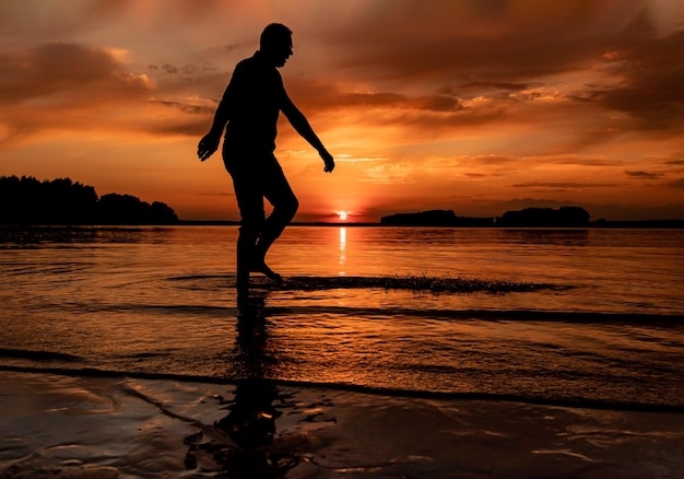 Silhueta ao pôr do sol no mar do lago homem caminhando à beira-mar bela vista do pôr do sol com céu laranja harmonia calma natureza beleza conceito