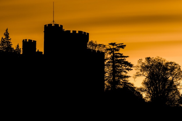 Silhueta assustador de um castelo e árvores com céu laranja