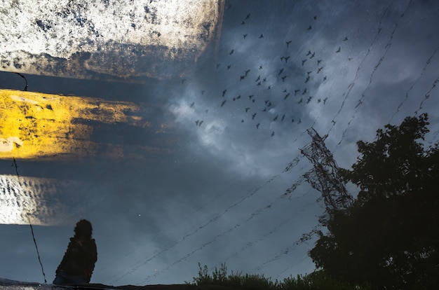 Silhueta borrada do reflexo de uma pessoa caminhando sozinha na calçada molhada da cidade em um dia chuvoso