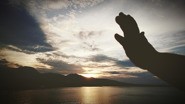 Silhueta cortada de la mano de una persona junto al lago contra el cielo durante la puesta de sol