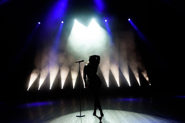 Foto silhueta da cantora no palco. fundo escuro, fumaça, holofotes.